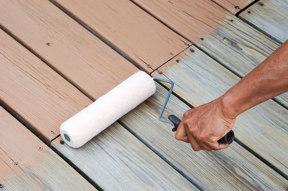 Fresh coat of exterior paint being applied to a wooden deck with a paint roller.
