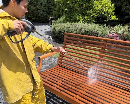 Professional contractor pressure washing teak outdoor furniture before refinishing.
