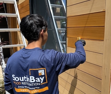 Professional contractor applying stain during an exterior wood siding refinishing project